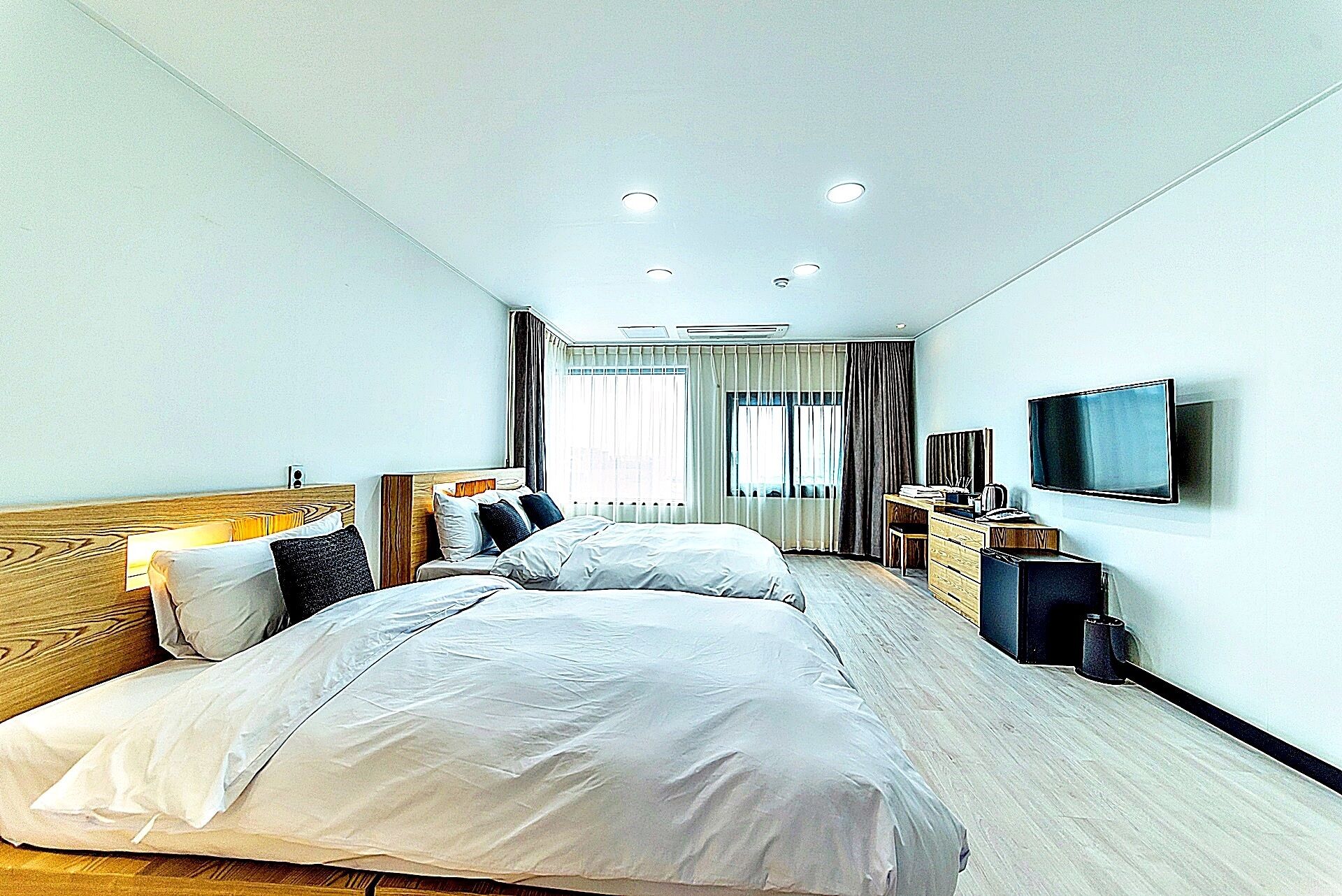 A hotel room with two beds, a TV, a desk, and a window with curtains.