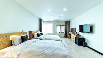A hotel room with two beds, a TV, a desk, and a window with curtains.