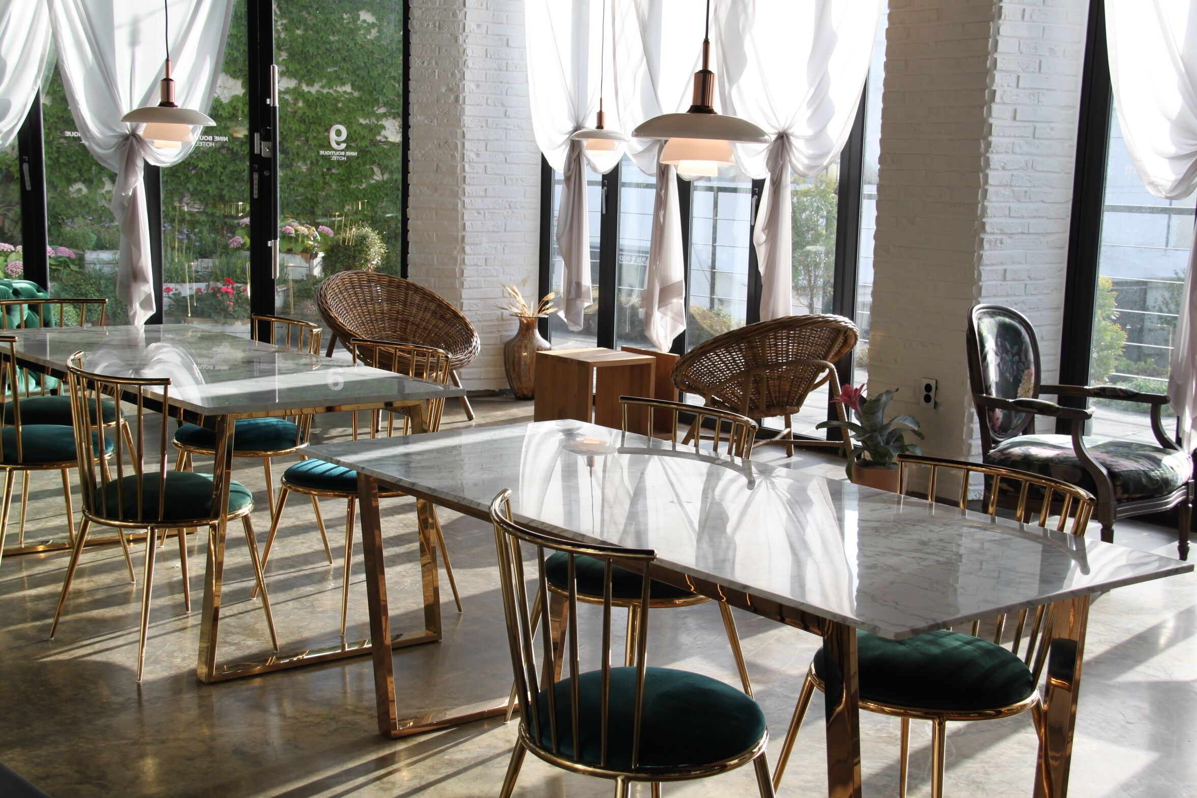A dining area with a long table, chairs with gold frames and green cushions, and pendant lights.