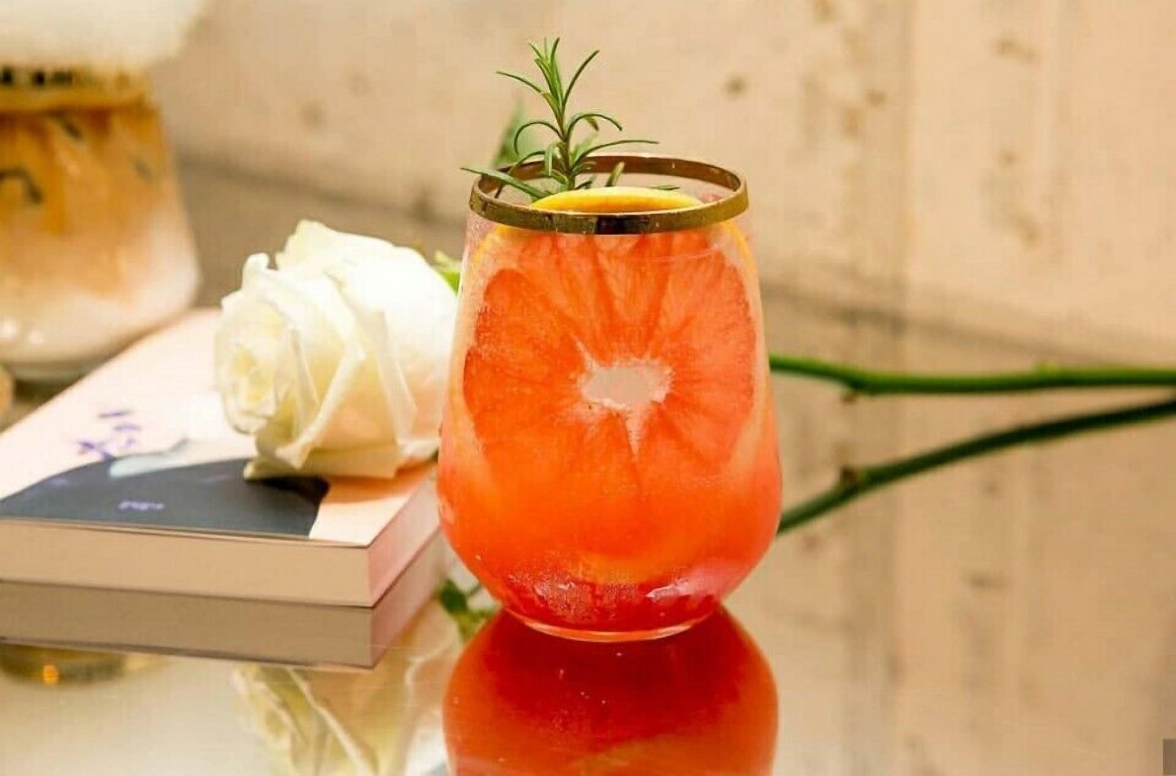 A glass with a slice of orange and a sprig of rosemary on a reflective surface.