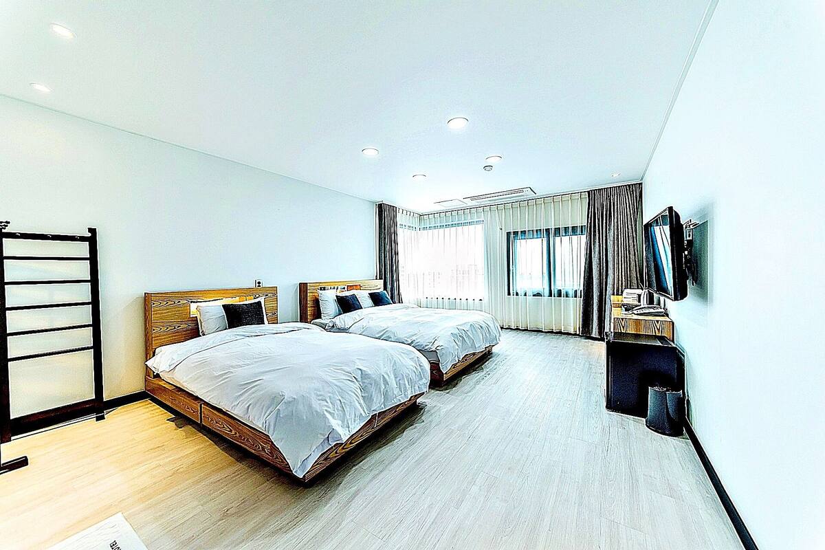 Una habitación de hotel moderna con dos camas, un escritorio con computadora y un televisor.