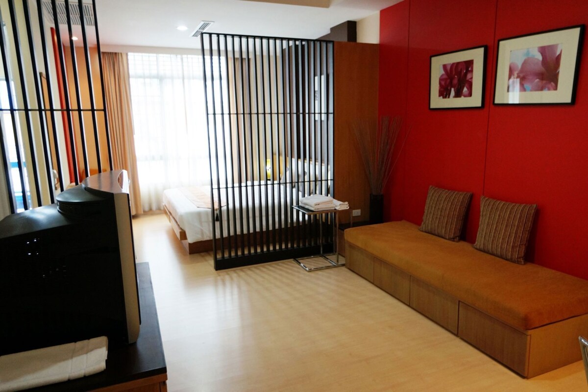 A modern room with a bed, a sofa, a TV, and a red wall with framed pictures.