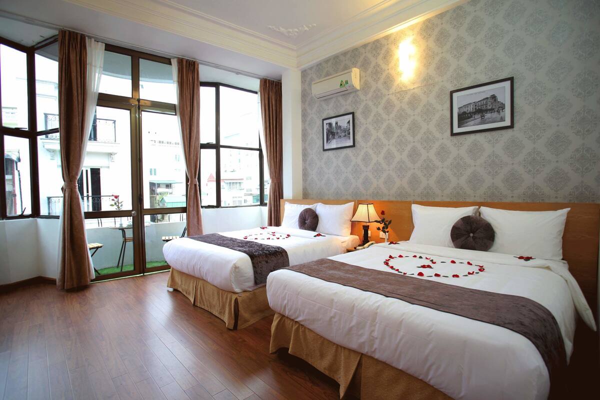 Habitació d'hotel amb dos llits, una finestra gran amb cortines, un aire condicionat fixat a la paret i un quadre encimbellat.