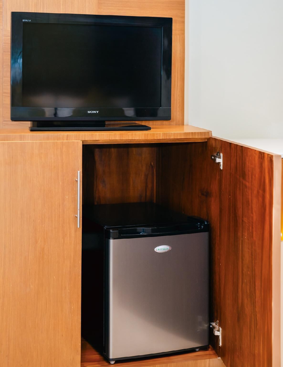 Una cocina compacta con refrigerador integrado y un televisor de pantalla plana montado sobre un mueble de madera.