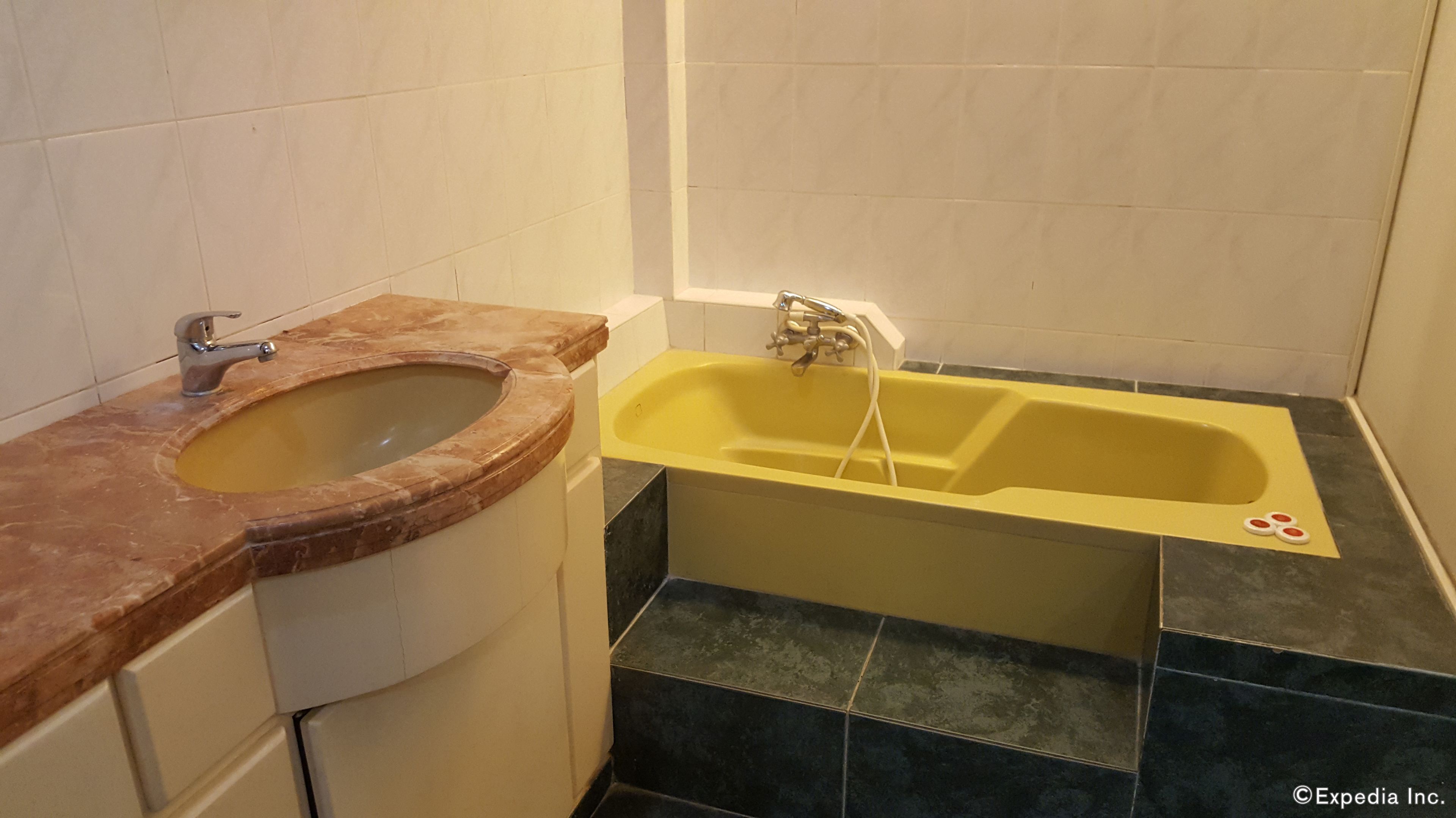 A bathroom with a marble sink, a yellow bathtub, and black tiles.