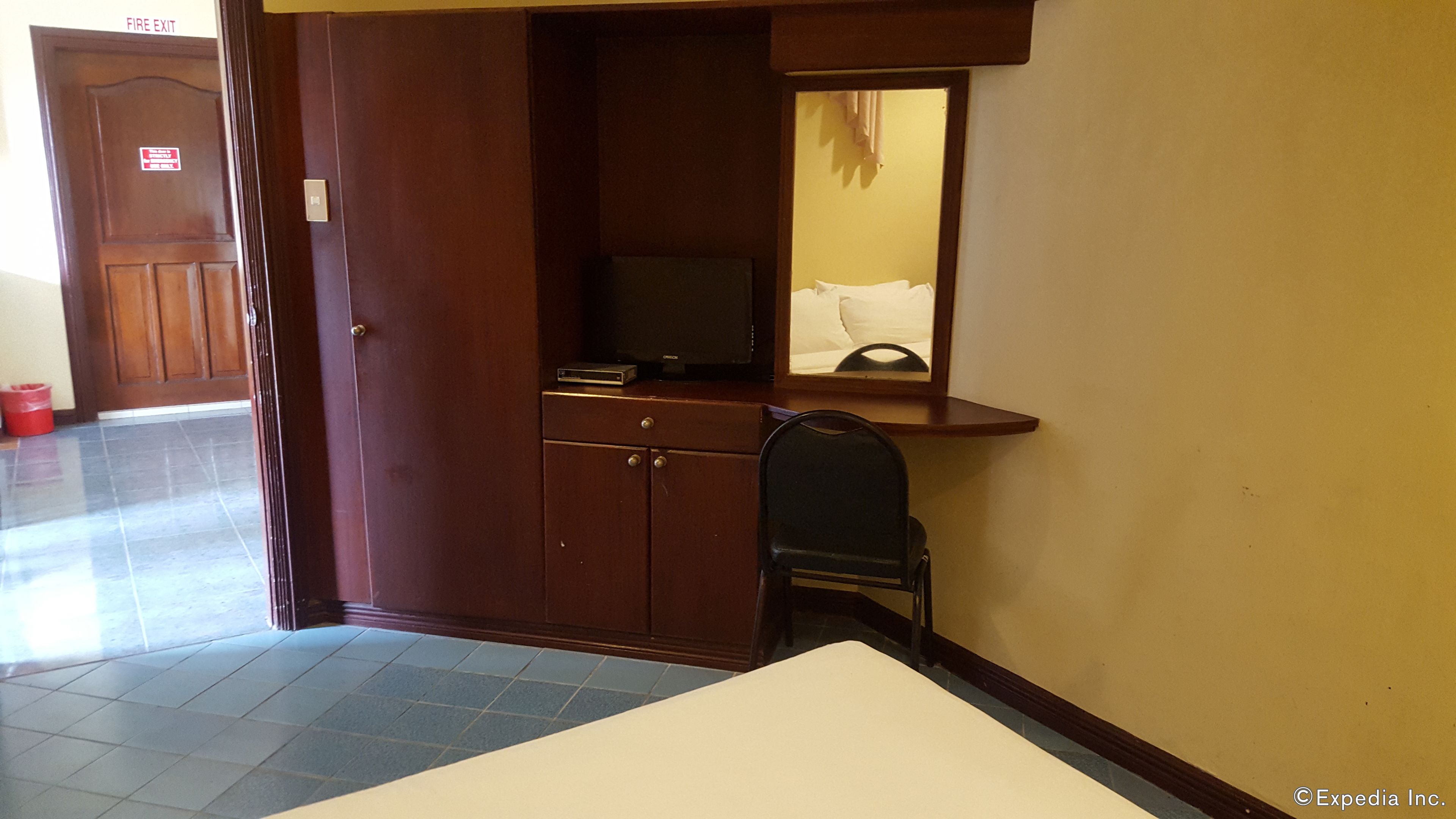 Habitación de hotel con un armario de madera, un televisor pequeño, un espejo y una silla.