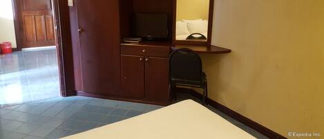Habitación de hotel con un armario de madera, un televisor pequeño, un espejo y una silla.