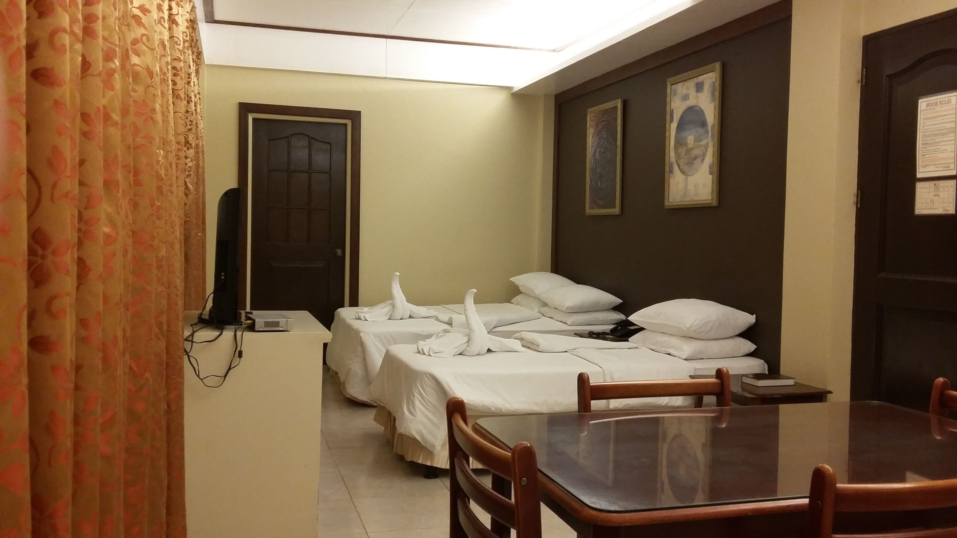 A hotel room with two beds, a dining table, chairs, a television, and a door with a window.