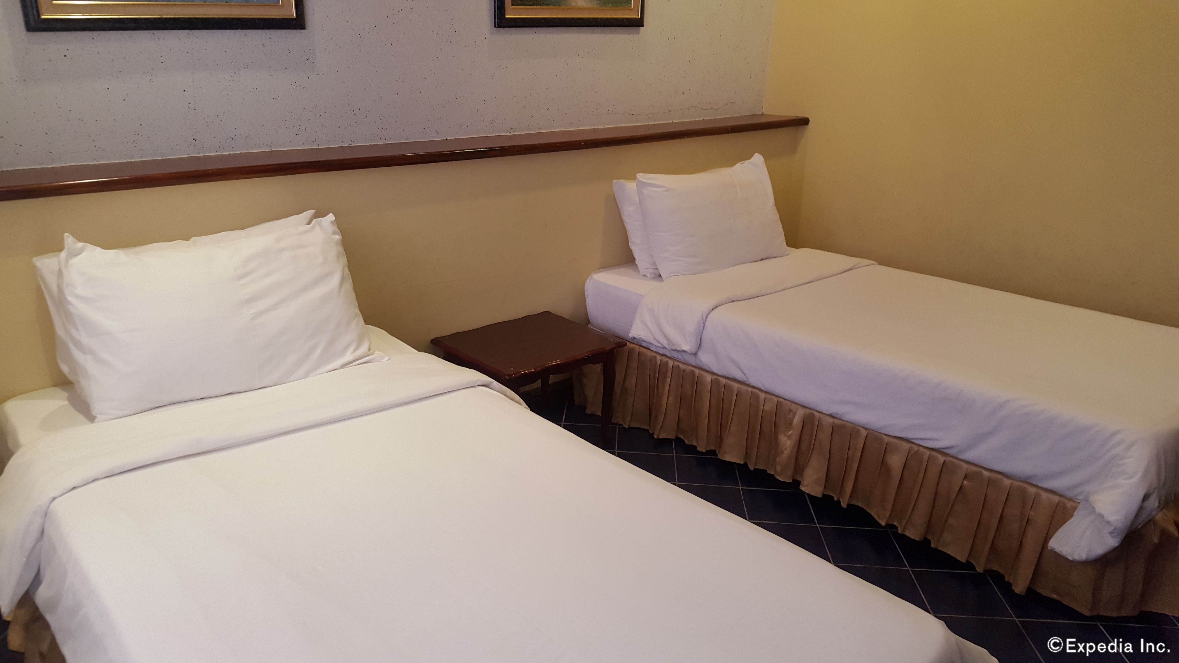 Two single beds with white linens, a wooden nightstand, and a wall-mounted shelf.