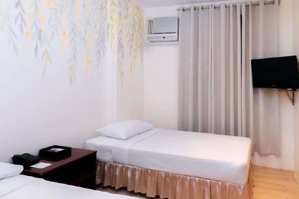 A hotel room with two beds, a flat-screen TV mounted on the wall, a bedside table with a phone, and a wall-mounted air conditioner.
