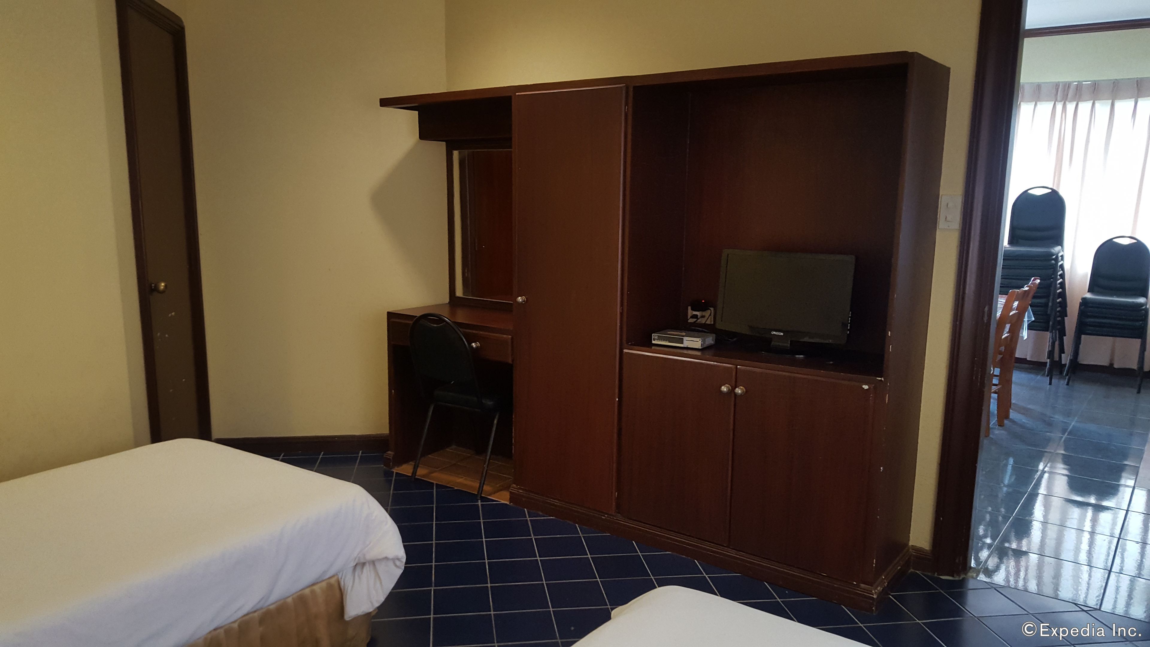 Une chambre d’hôtel avec deux lits simples, une armoire en bois, un bureau avec une télévision et une chaise.