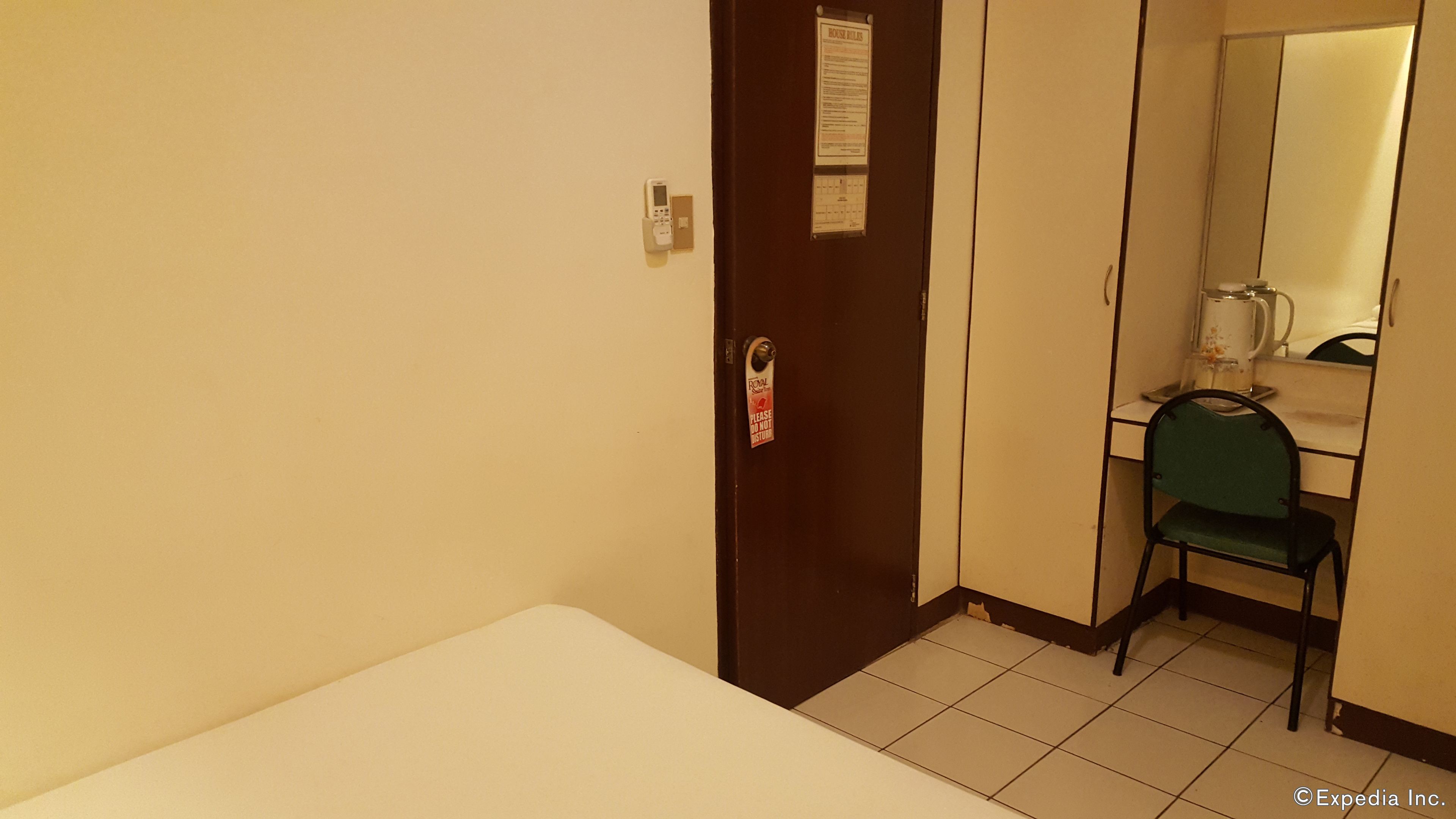 Une chambre d’hôtel avec un lit simple, un bureau avec une chaise, un miroir et une porte avec une pancarte.