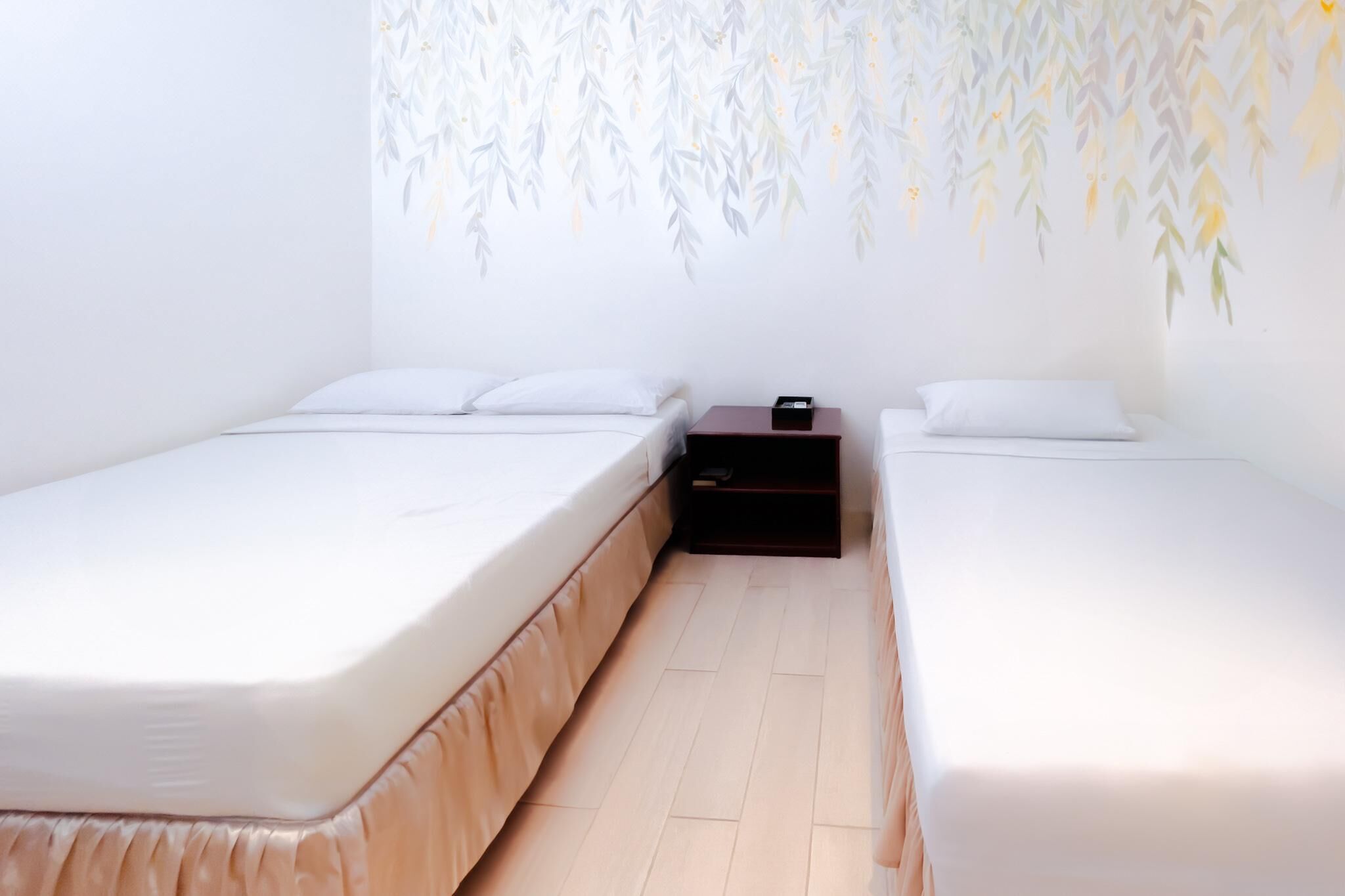 A room with two single beds, a small wooden nightstand, and a wall with a bamboo leaf pattern.