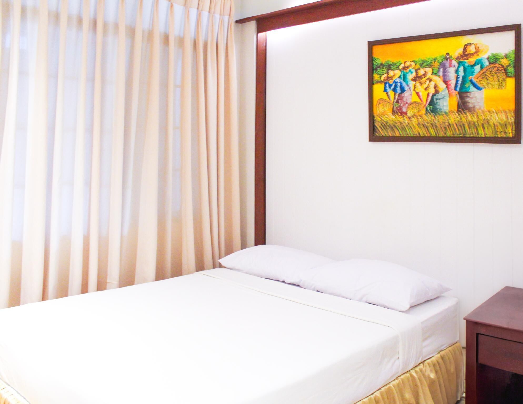 A hotel room with a bed, a wooden nightstand, and a painting on the wall.