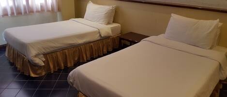 Una habitación de hotel con dos camas individuales, una mesita y una ventana con cortinas.