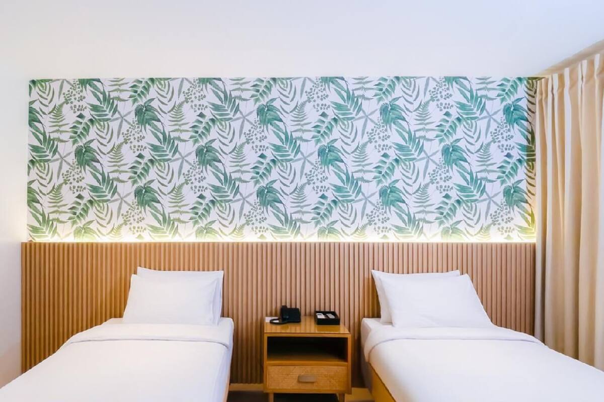 A hotel room with two beds, a wooden headboard, a nightstand, and a wall with a leafy pattern.