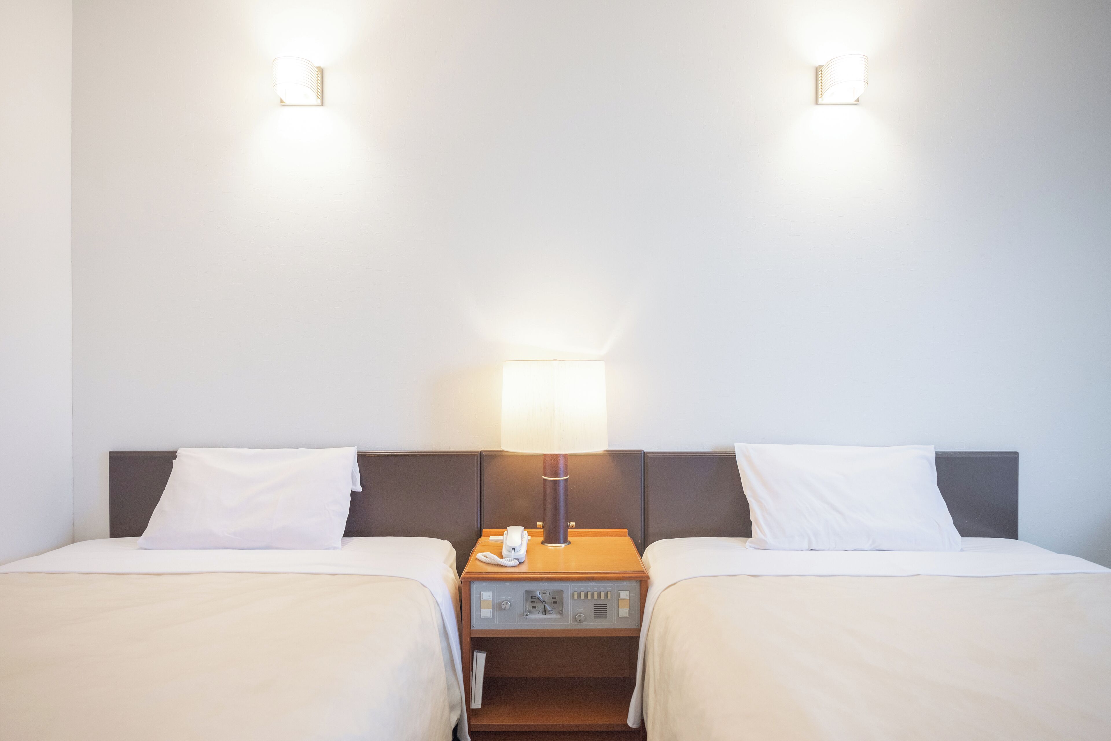 A hotel room with two beds, a nightstand with a lamp, and a phone.