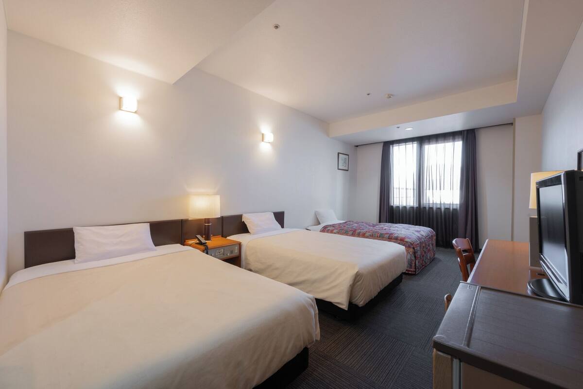 Une chambre d’hôtel avec deux lits, un bureau, une télévision et une fenêtre avec des rideaux.