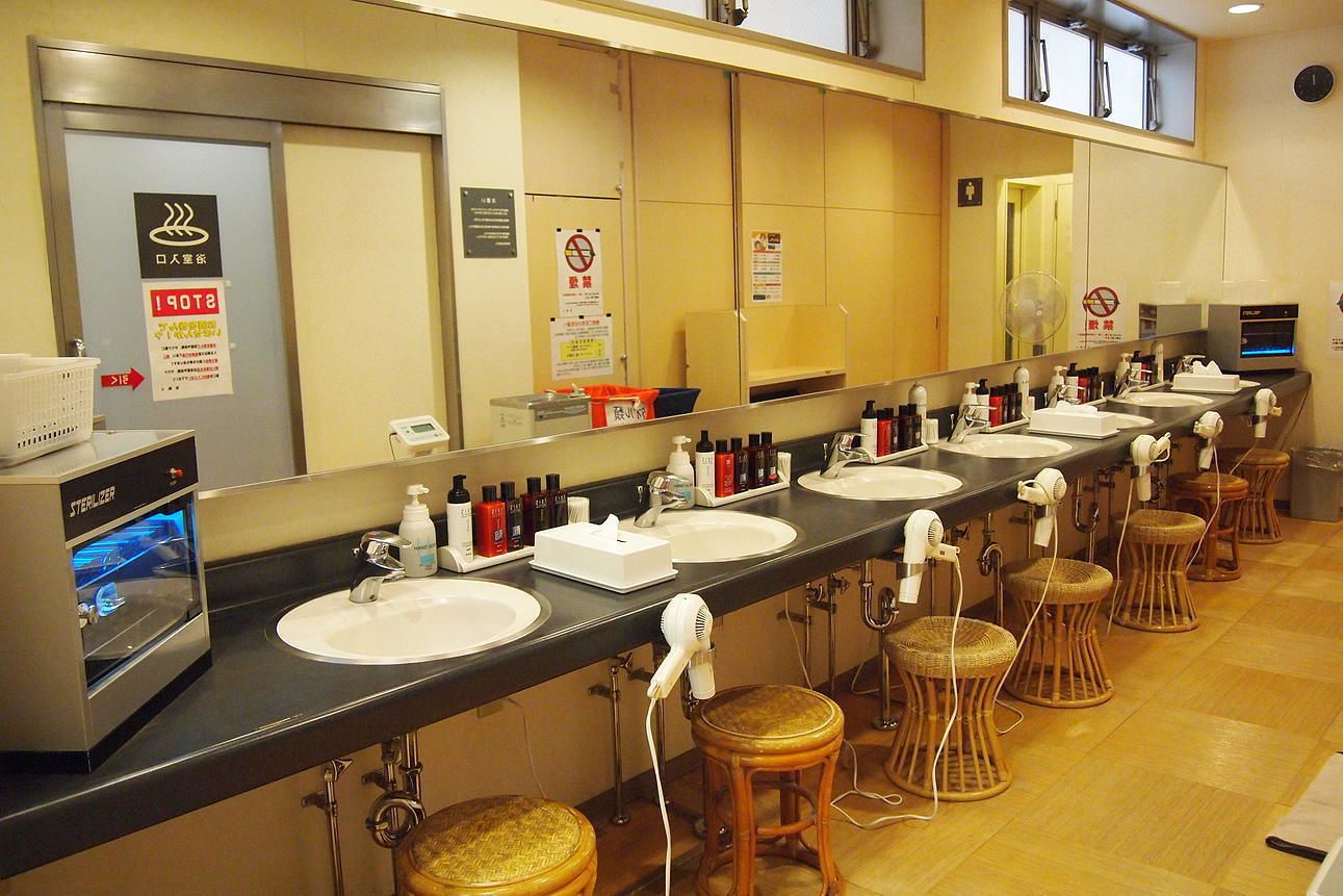 A row of sinks with mirrors, hair dryers, and toiletries.