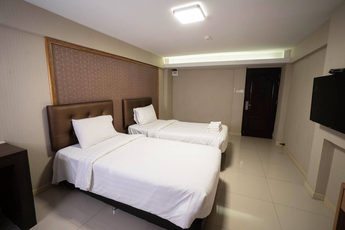 A hotel room with two beds, a flat-screen TV, and a door leading to another room.