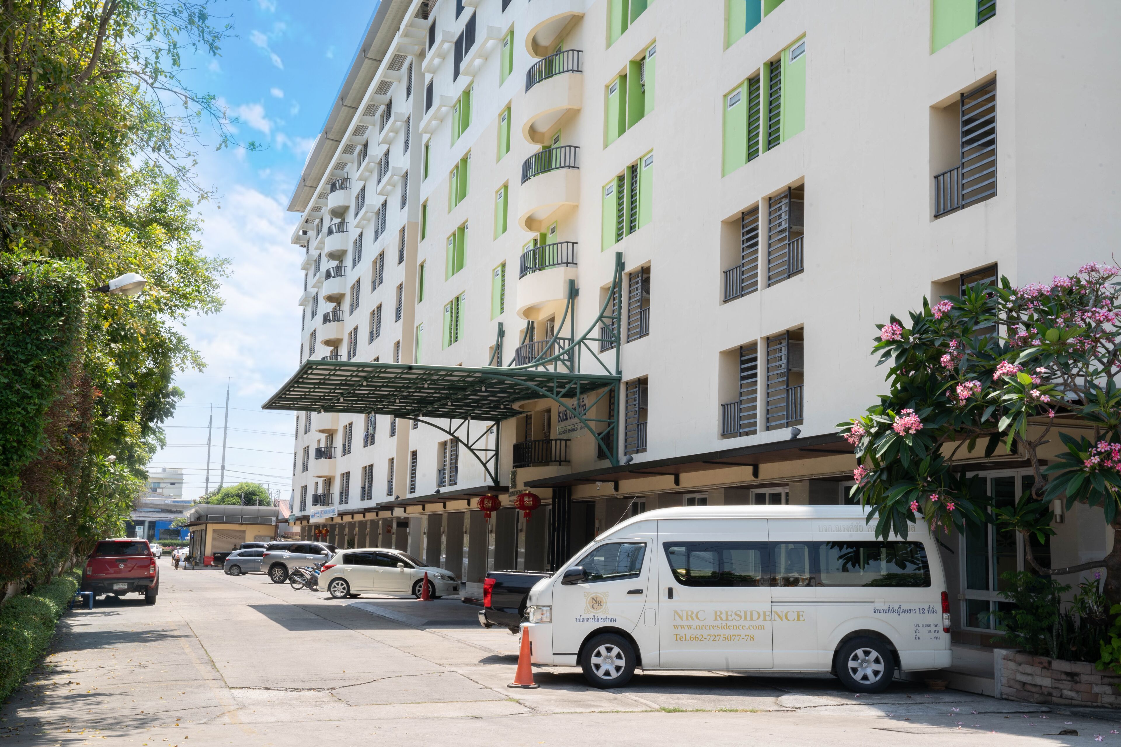 A multi-story hotel with balconies, a covered entrance, and a van parked in front.