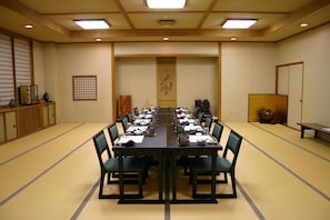 Un salón de conferencias con una larga mesa, sillas y varios objetos como teteras y tazas.