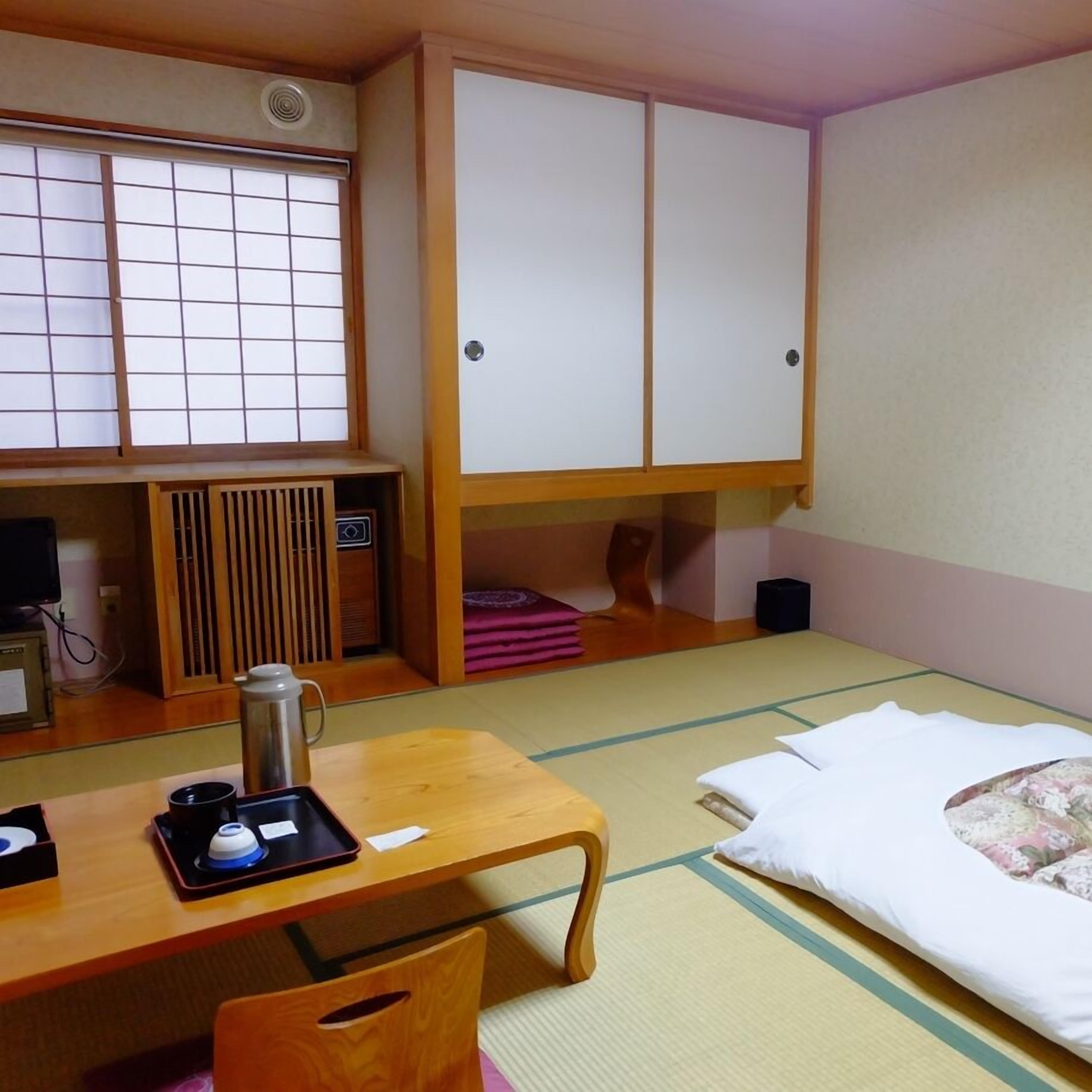 A room with tatami flooring, a desk with a kettle, a bed with a pillow, and a wardrobe.