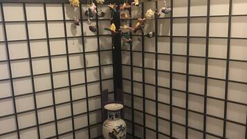 A decorative vase with a bird design on a pedestal in a corner with a grid-patterned wall.