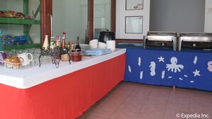 A buffet setup with a red tablecloth, various food containers, and a blue tablecloth with white decorations. - Planet Dive (Mabini)