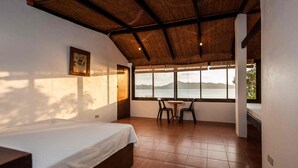 A bedroom with a bed, a window with a view of the water, and a table with chairs. - Planet Dive (Mabini)