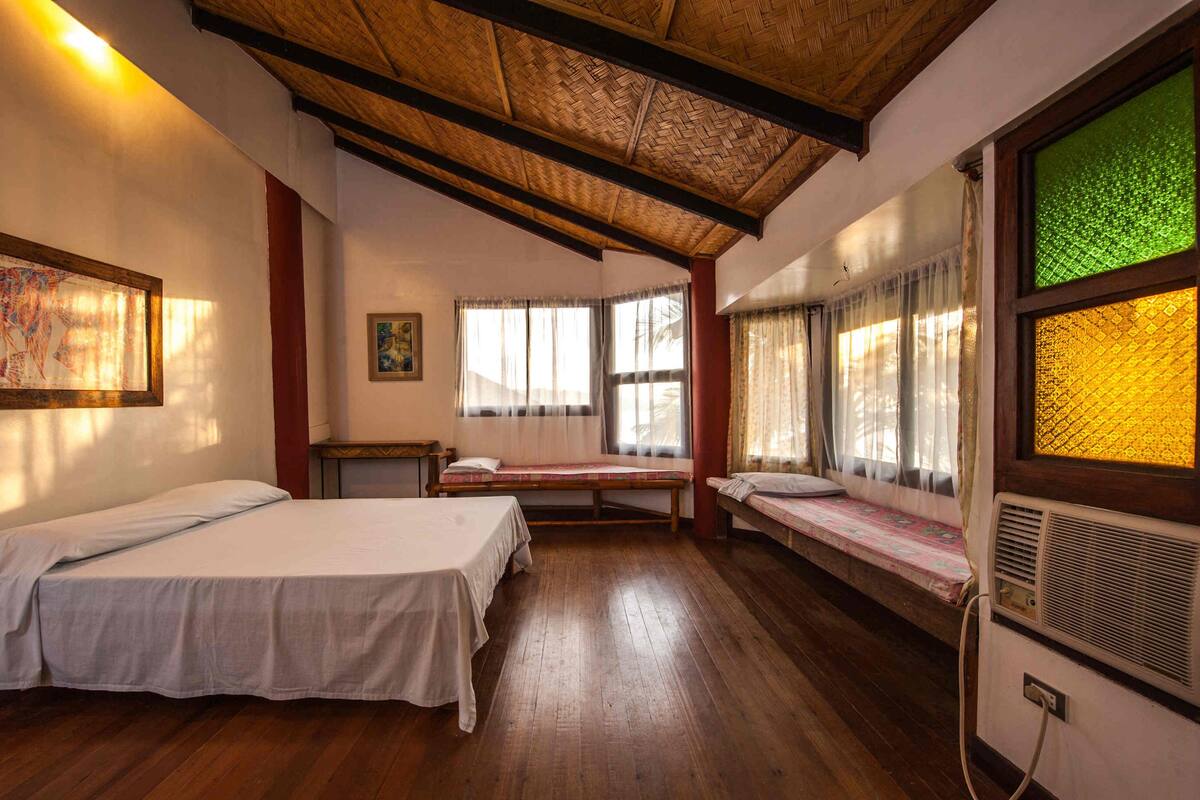 A room with two beds, a wooden ceiling, and a window with a green-tinted glass.