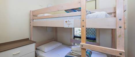 Una cama litera con estructura de madera, una mesita de noche pequeña y un módulo de cajones.