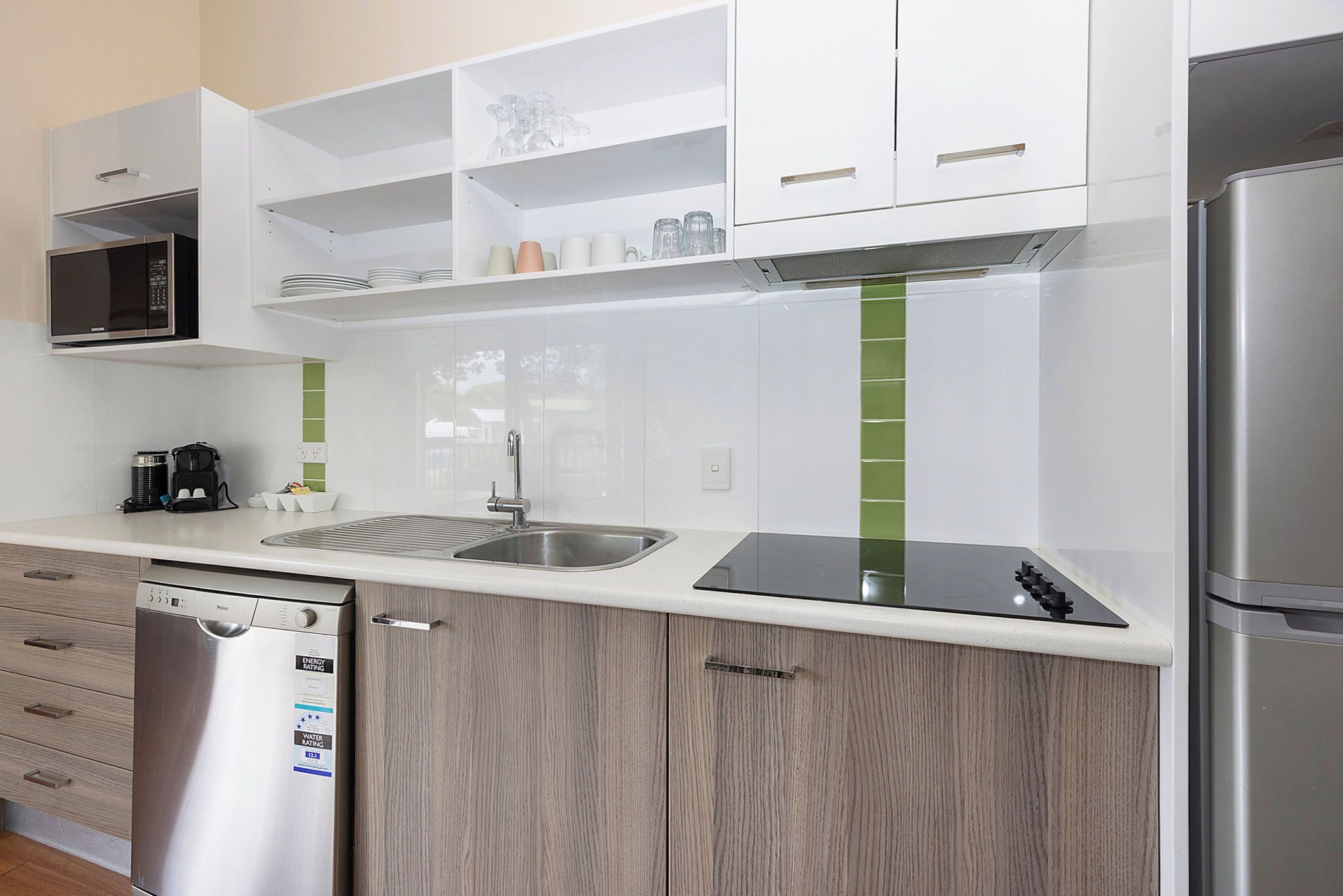 A modern kitchen with white cabinets, a stainless steel dishwasher, a microwave, and a refrigerator.