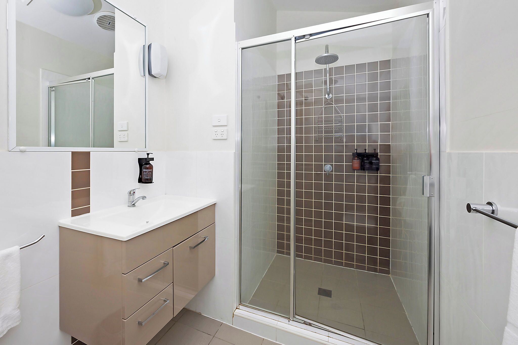 A modern bathroom with a glass-enclosed shower, a white sink with a mirror above it, and a beige vanity with drawers.
