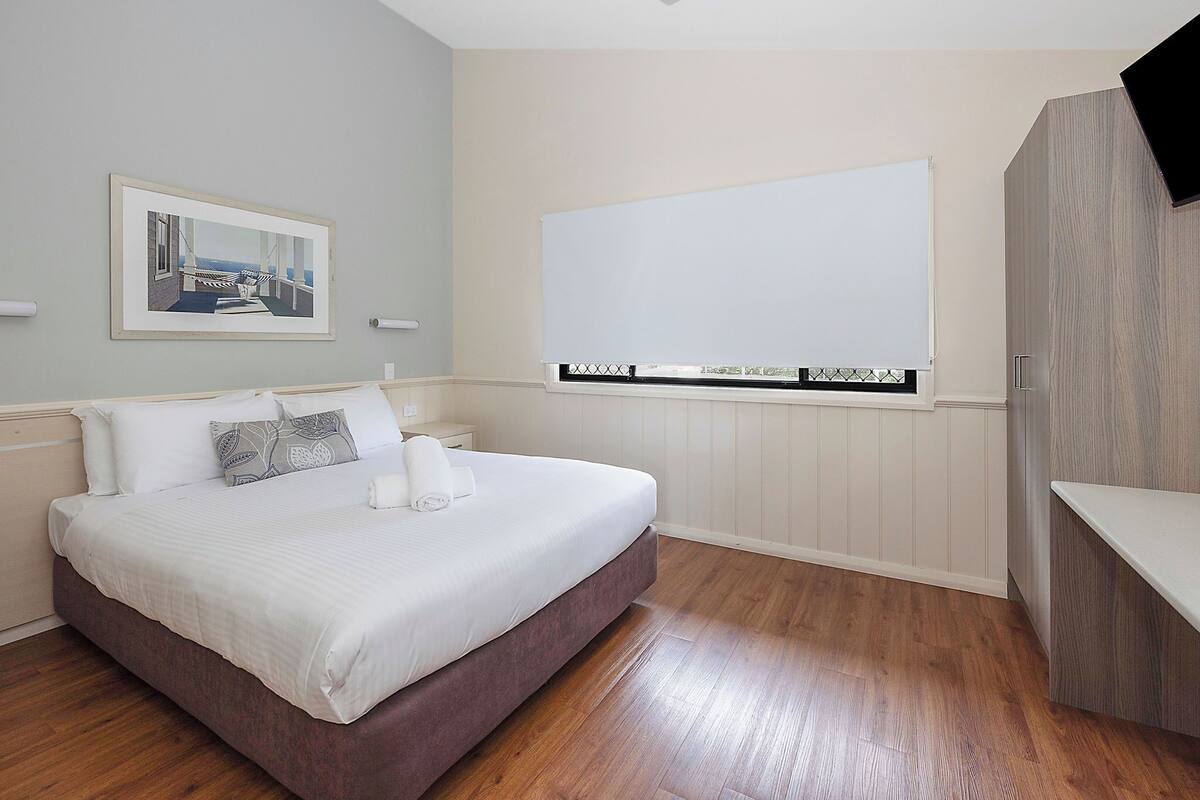 A bedroom with a bed, a large window, and a mounted TV.