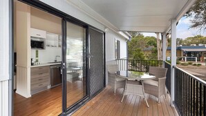 A modern balcony with a dining area, a sliding glass door leading to a kitchen, and a view of the street. - Reflections Eden - Holiday Park (Eden)