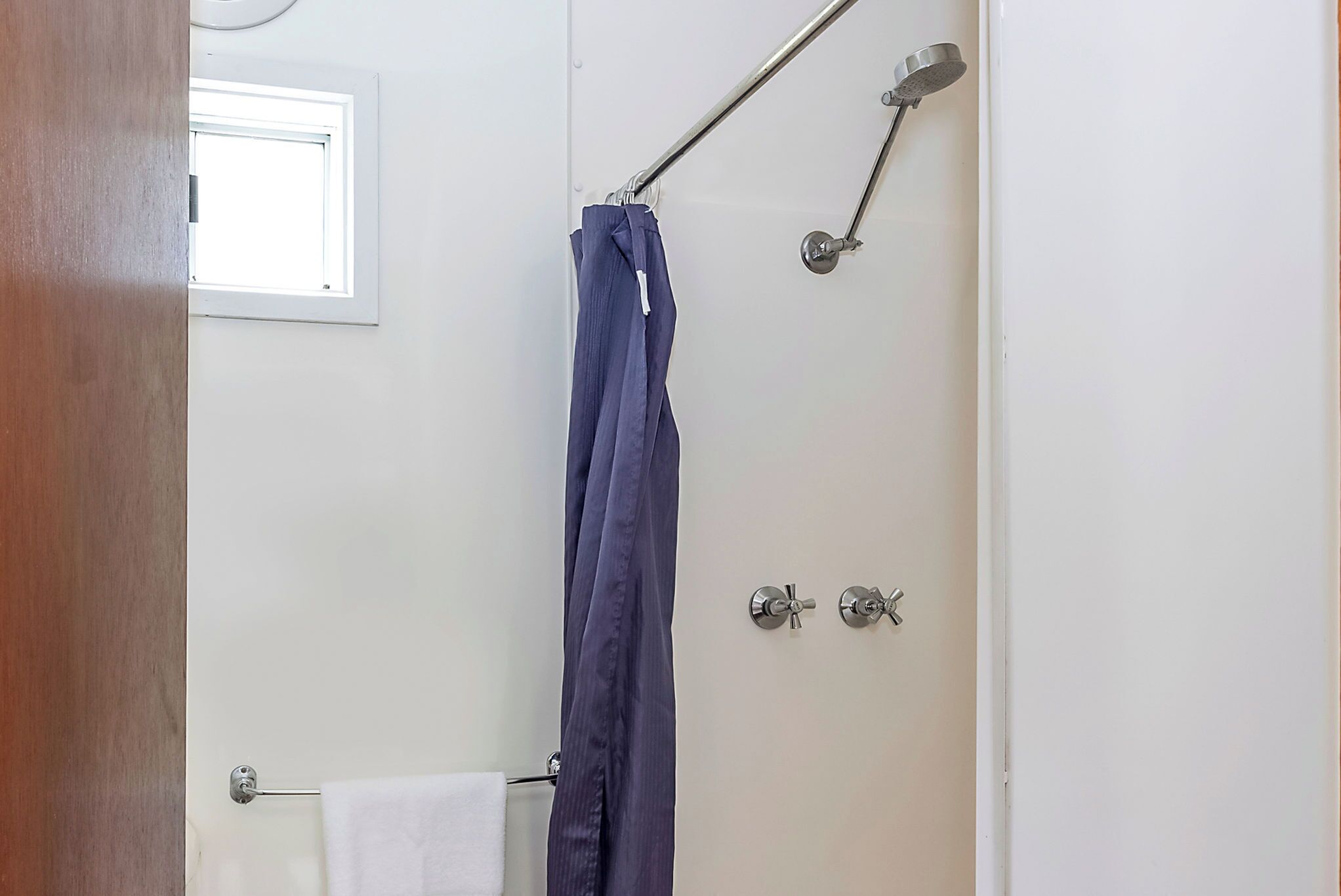 A bathroom with a shower curtain, a towel rack, and a window.