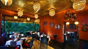A restaurant with wicker chairs, tables with white tablecloths, and hanging wicker lamps. - Petit Hotel Bali (Ubud)