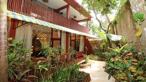 A building with a covered balcony, surrounded by lush greenery and plants. - Petit Hotel Bali (Ubud)
