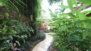 A narrow, curved water channel surrounded by lush greenery and a stone wall. - Petit Hotel Bali (Ubud)