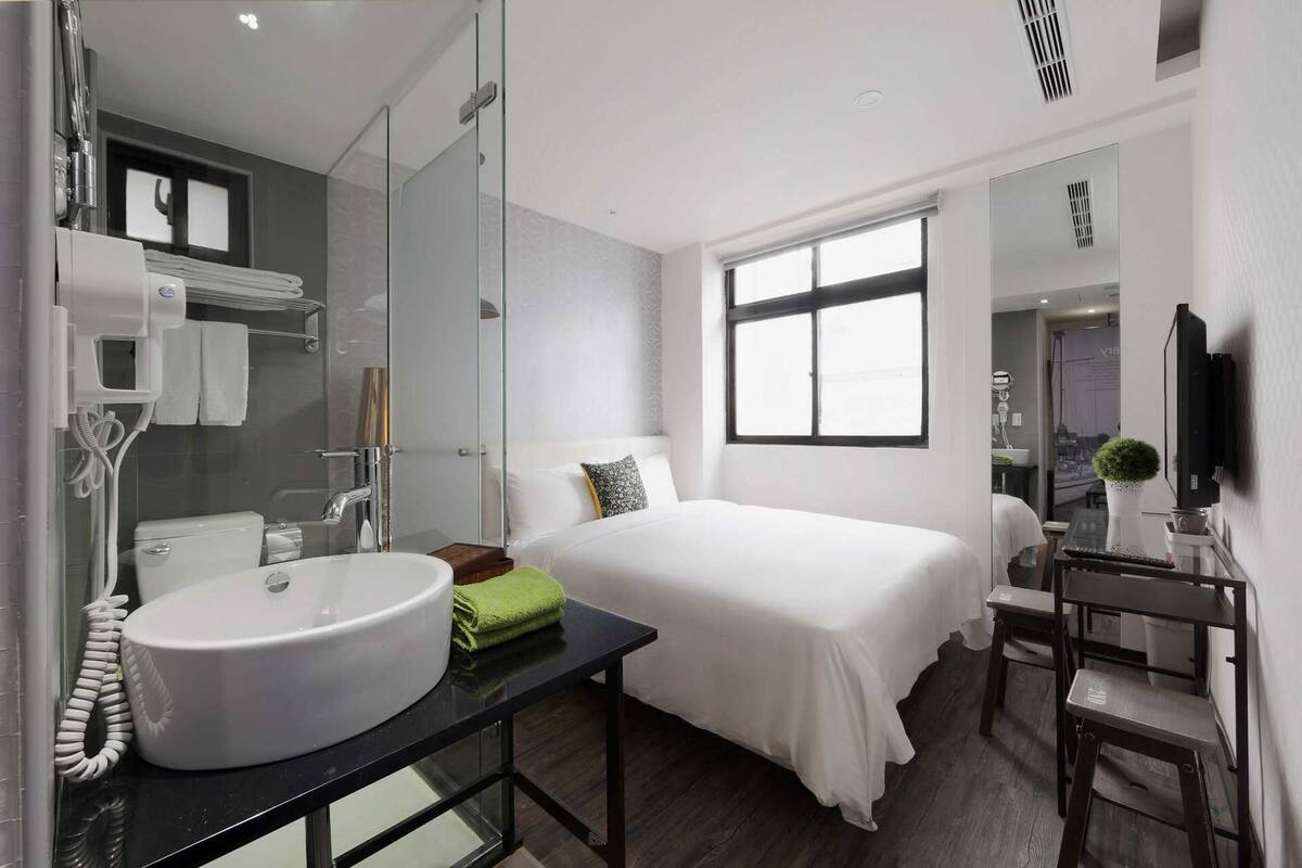 Habitación de hotel moderna con una cama grande, una mesita de noche, un espejo, un lavamanos y una televisión.