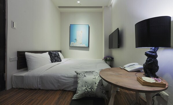 Habitación de hotel con una cama, una mesita de noche con lámpara, un teléfono y un cuadro en la pared.