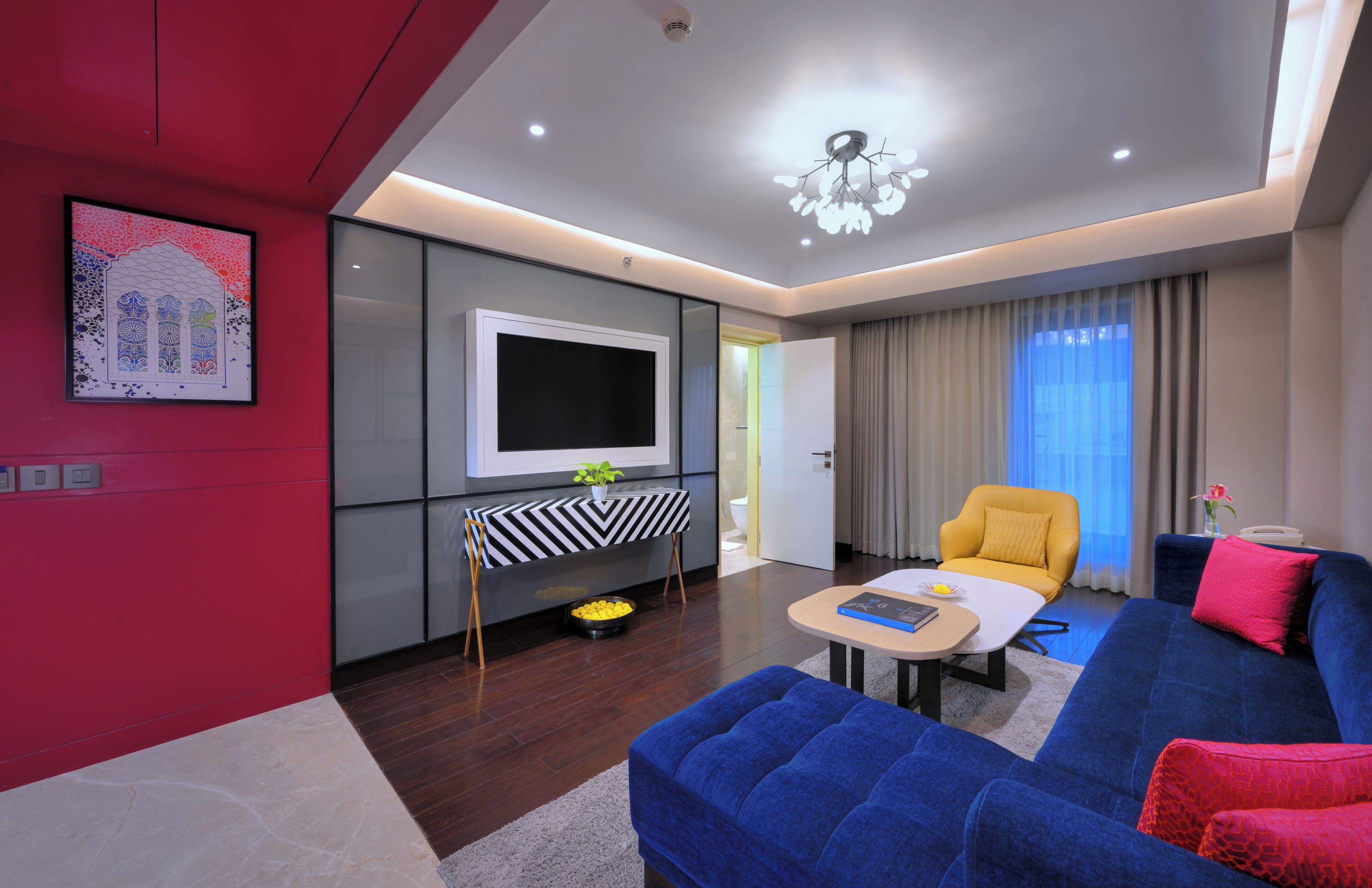 Una sala moderna con un sofá azul, un sillón amarillo, un televisor de pantalla plana y una mesita con una planta.