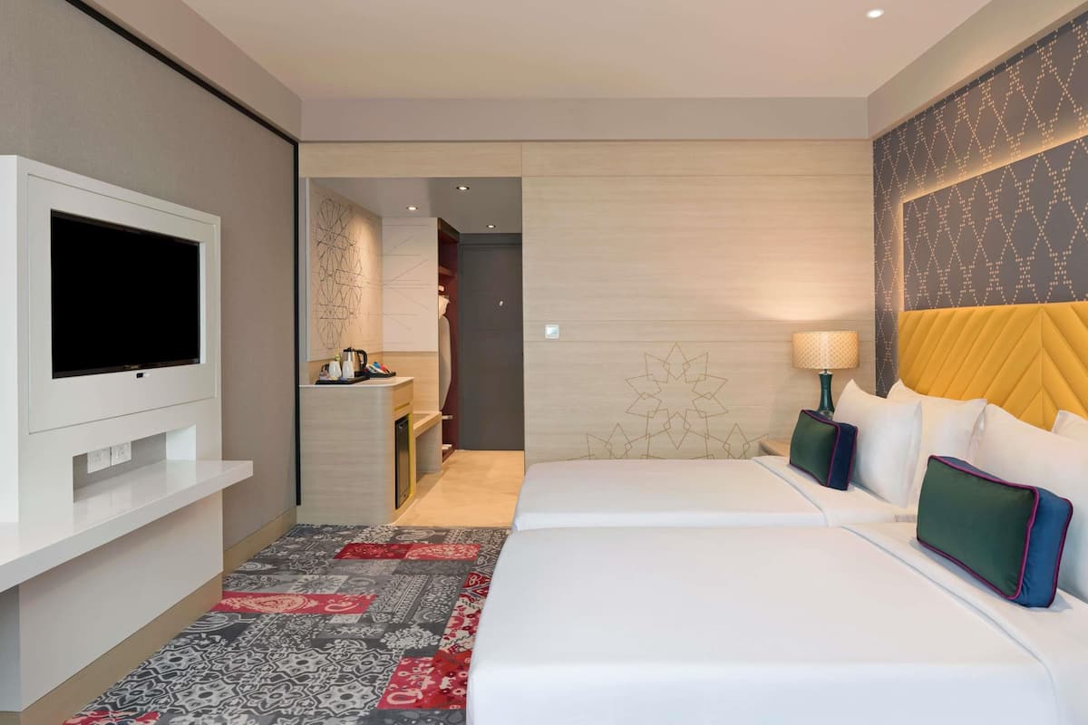 A hotel room with a flat-screen TV, a bed with white bedding, a patterned rug, and a decorative wall panel.