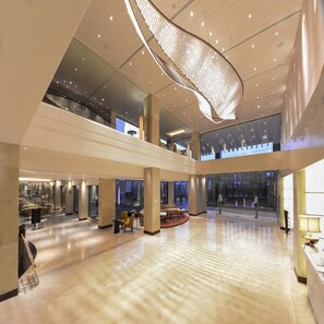 A spacious lobby with a high ceiling, a central seating area, and a view of the lower level through glass walls. - Grand Mercure Agra (Agra)