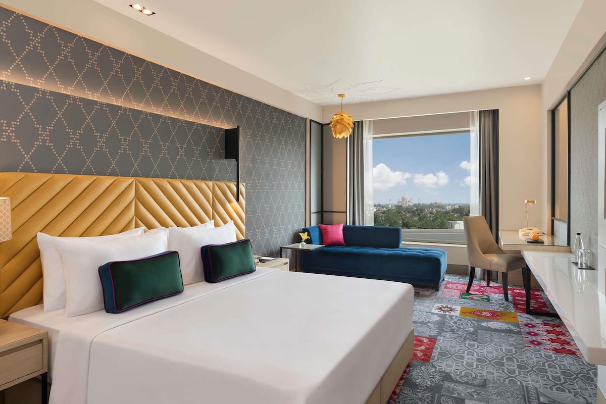 A hotel room with a large bed, a desk, a chair, and a view of the city.