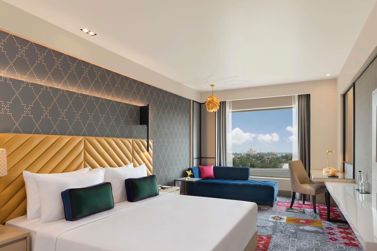 Habitación de hotel con una cama grande, un escritorio, una silla y vistas a un paisaje urbano.