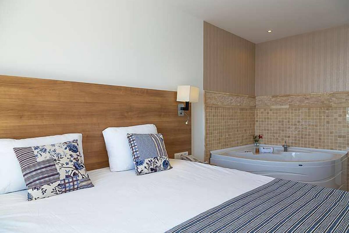 A hotel room with a large bed, a wooden headboard, a wall-mounted lamp, and a bathtub.