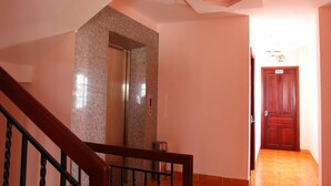Un couloir avec un escalier en bois, un ascenseur en granit et une porte en bois portant le numéro 401.