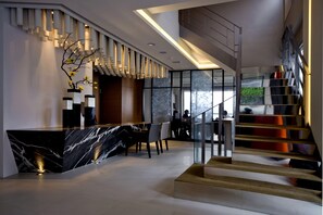 Un moderno vestíbulo de hotel con una recepción de mármol, una escalera con barandillas de vidrio y vistas al exterior.
